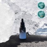 AK PURE SKIN Hydrating Serum bottle standing on black volcanic sand with glistening ice in the background, captured outdoors in Icelandic nature.